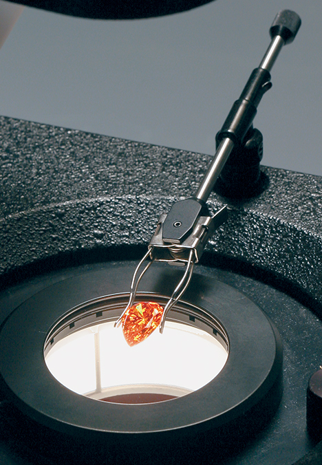 Synthetic orange sapphire held by clamp over a darkfield microscope Synthetic orange sapphire held by clamp over a darkfield microscope