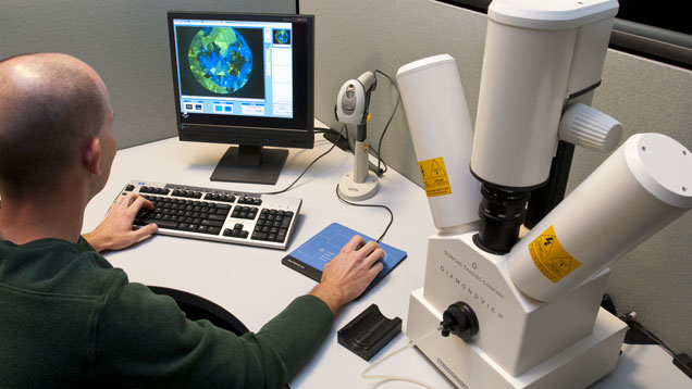 A person is working at a computer with a microscope setup, analyzing data displayed on the screen. A person is working at a computer with a microscope setup, analyzing data displayed on the screen.