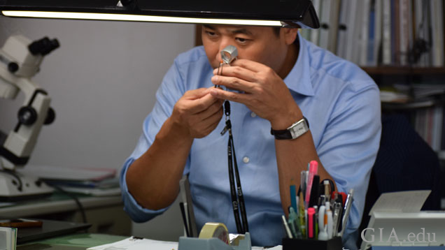 Ken Fujita(藤田健)博士使用放大镜在办公桌上检查宝石。 Ken Fujita(藤田健)博士使用放大镜在办公桌上检查宝石。