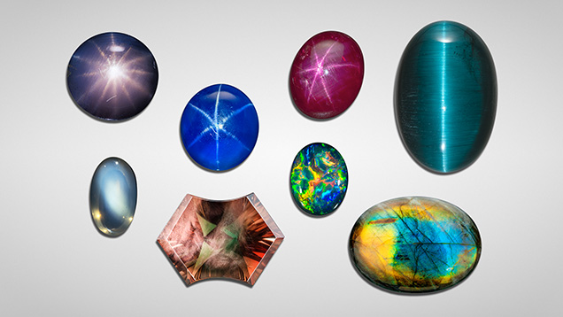 A collection of various gemstones in different shapes and colors, including blues, greens, and purples, displayed on a light background.